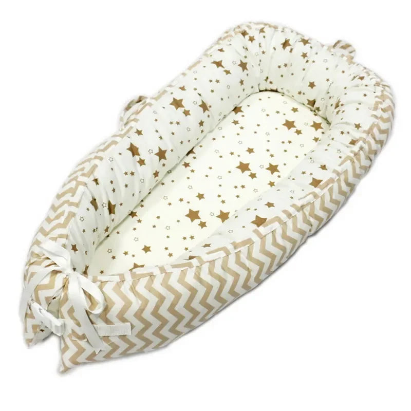 Infant nest sleeper with beige zigzag sides and white interior printed with brown stars, featuring soft padded edges and tied with white ribbons at the bottom.