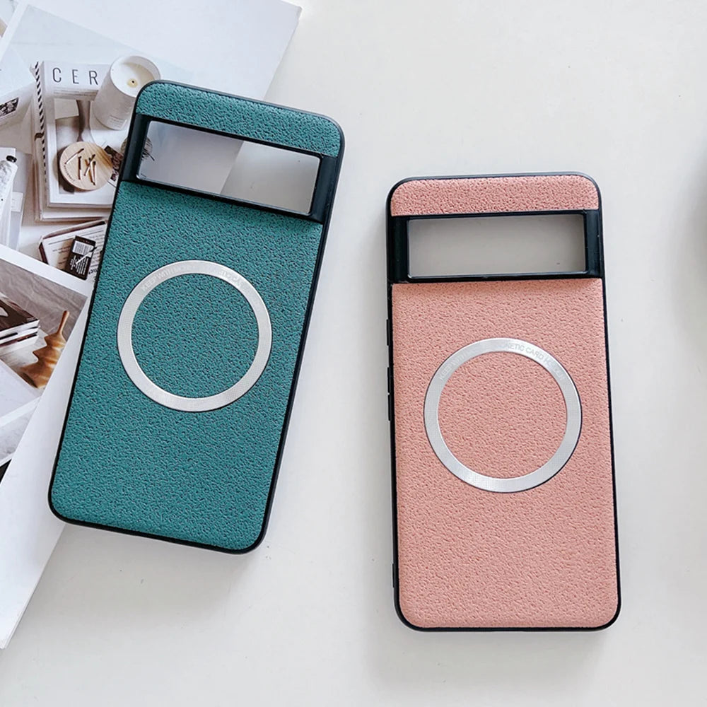 Two smartphone cases with a textured finish and circular metal accents are displayed, one in teal and the other in pink, placed on a white surface near magazines.