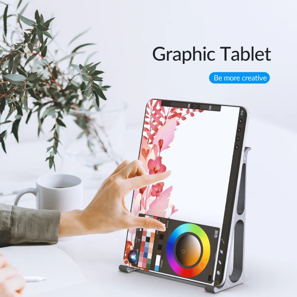 A person uses a graphic tablet to draw pink flowers on a white canvas, with a plant, notebook, and coffee cup in the background. The text reads "Graphic Tablet - Be more creative."