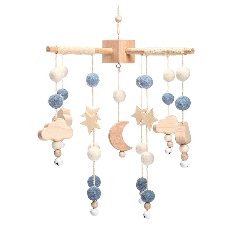A wooden baby mobile featuring hanging felt balls in blue and white, with wooden shapes of stars, a crescent moon, clouds, and a car, suspended from wooden rods.
