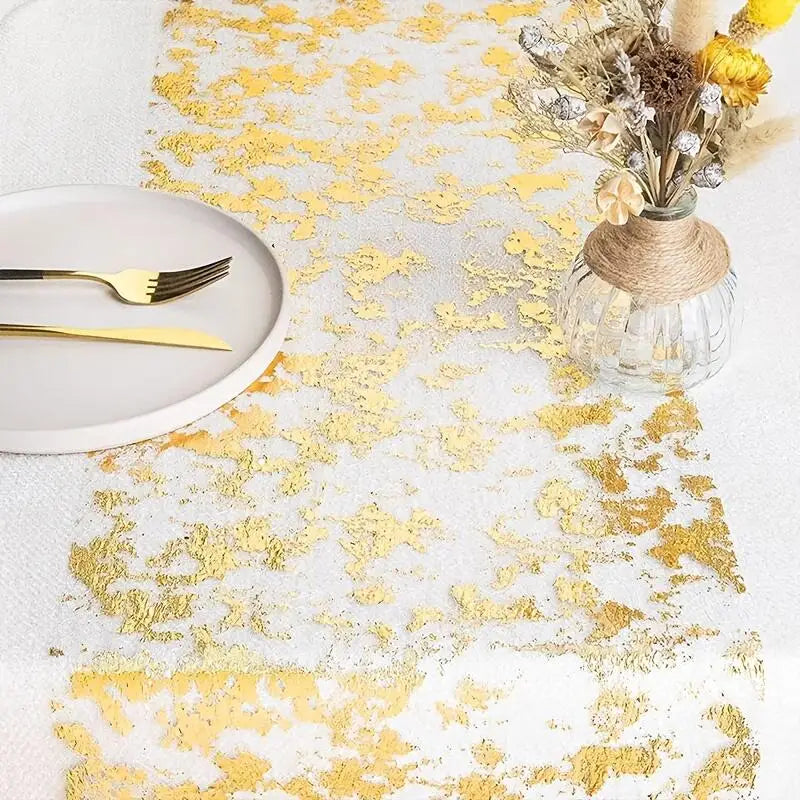 Elegant table setting with a white and gold textured runner, a plate with gold utensils, and a vase of dried flowers wrapped in jute, creating a sophisticated ambiance.