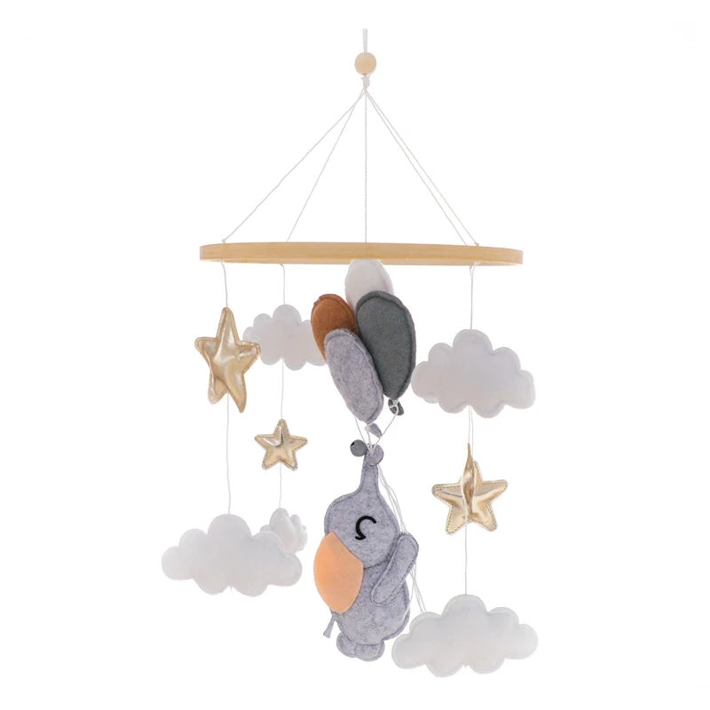 Nursery mobile featuring felt stars, clouds, and a sleeping bird hanging from a wooden frame. The soft colors include gray, white, orange, and gold, creating a calming atmosphere.