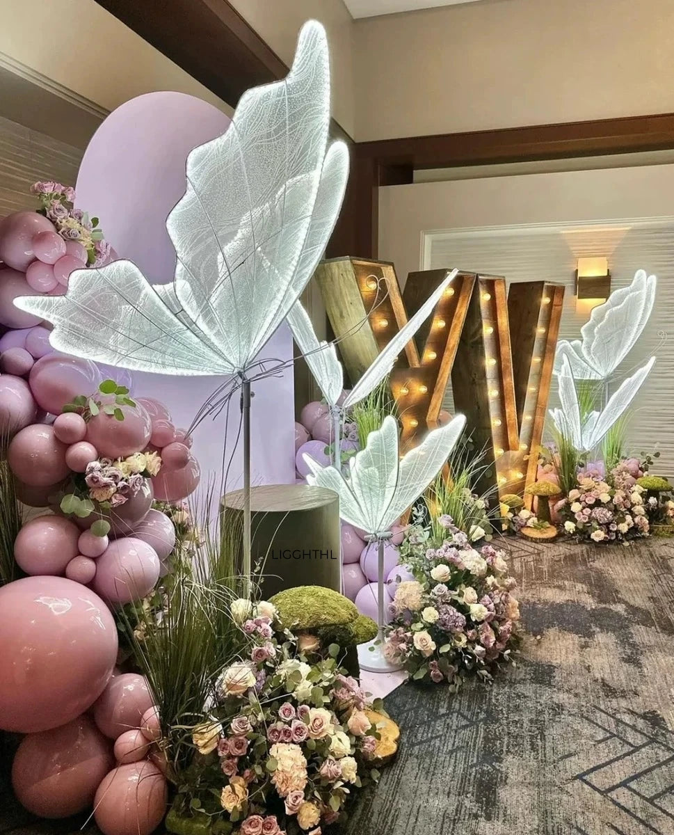 Elegant party decor with pink balloons, glowing leaf sculptures, floral arrangements, greenery, and illuminated "XV" letters, creating a whimsical and festive atmosphere.