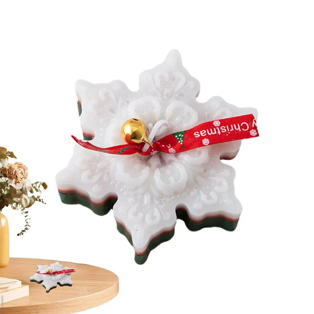 White snowflake-shaped soap with ornate details, tied with a red "Merry Christmas" ribbon and a small gold bell, placed on a wooden table with a floral arrangement.