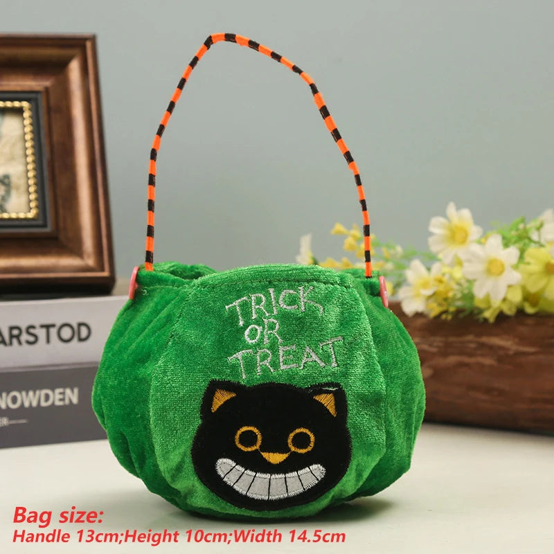 Green plush Halloween bag with "Trick or Treat" text and a smiling black cat face. Orange and black striped handle; size noted in red text. Background shows a plant and photo frame.