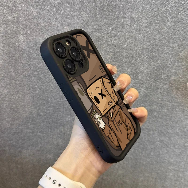 iPhone with a black case held in a hand with painted nails. The case has a cartoon of a person wearing a box mask with an "X" face, holding a cup, and wearing a hoodie.