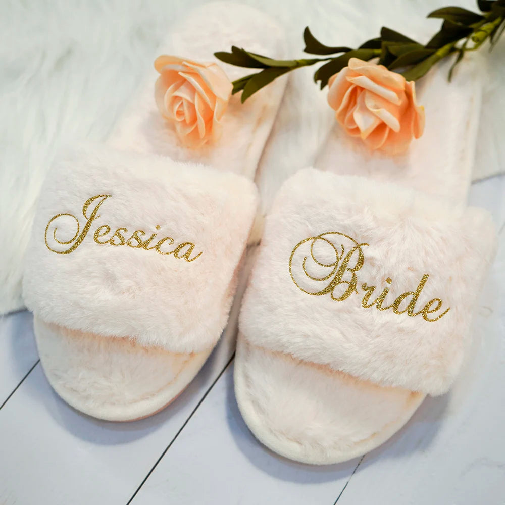 Fluffy white slippers with gold embroidery reading "Jessica" and "Bride." Each slipper is adorned with a soft peach rose on a white textured floor.