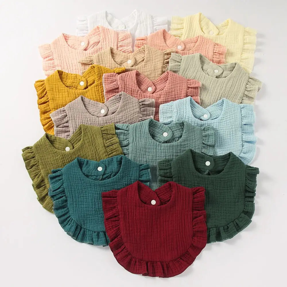 A collection of baby bibs in various colors, including yellow, pink, teal, and maroon, arranged in a neat pattern. Each bib features a ruffled edge and button closure.