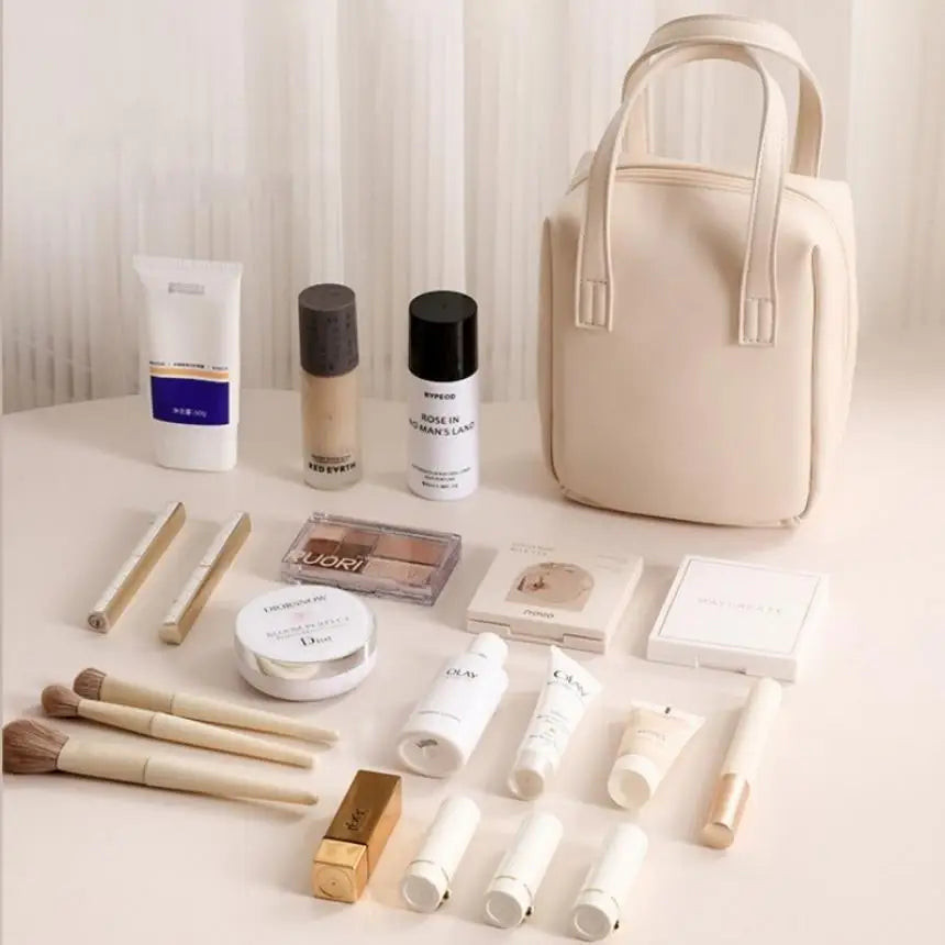A beige makeup bag surrounded by various beauty products, including foundation, face creams, brushes, lipsticks, and eyeshadow, all neatly organized on a soft cream surface.