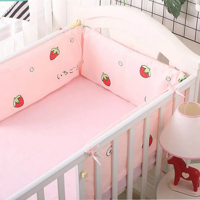 Pink crib with strawberry-printed bumpers, white railings, and a matching lamp and red horse figurine. A plant and grid-patterned wall are in the background.