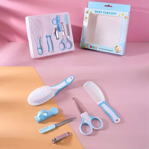 Baby care kit with blue and white grooming tools, including a brush, comb, scissors, clippers, file, and nasal aspirator. Packaging box in the background. Pink and beige surface.