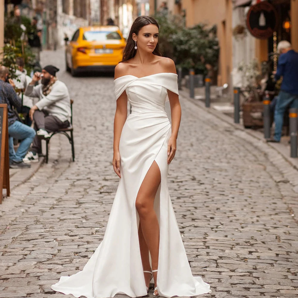 A woman in an elegant off-shoulder white gown with a thigh-high slit walks confidently down a cobblestone street. A yellow taxi and people are in the background.