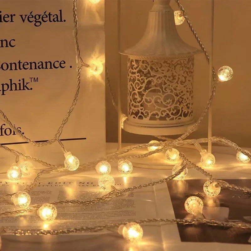 Warm white string lights draped around a decorative white lantern and paper bag, casting a cozy glow on an open magazine in a softly lit setting.