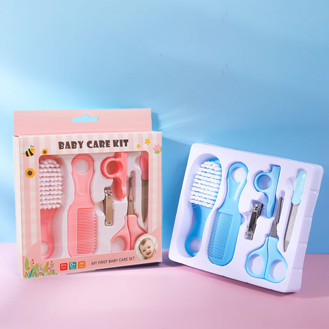 Baby care kit with pink and blue sets featuring a brush, comb, scissors, nail clippers, and dropper. The pink set is boxed; the blue set is displayed on a light purple surface.