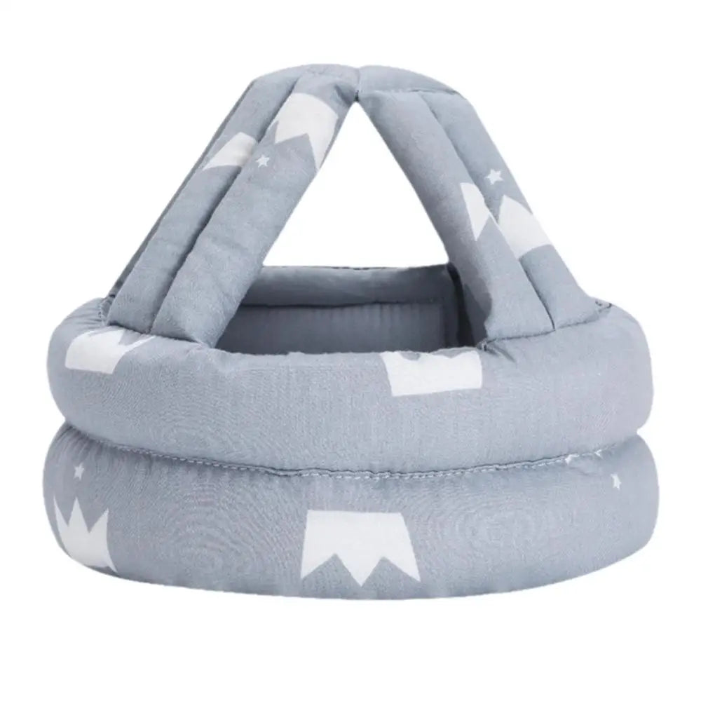 Soft, light gray baby head protector with a crown pattern and padded straps forming a triangular top, designed for toddler safety during walking or crawling.
