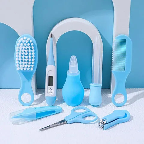 A set of blue baby grooming essentials against a blue and white backdrop, including a brush, thermometer, nasal aspirator, comb, dropper, tweezers, scissors, and nail clippers.