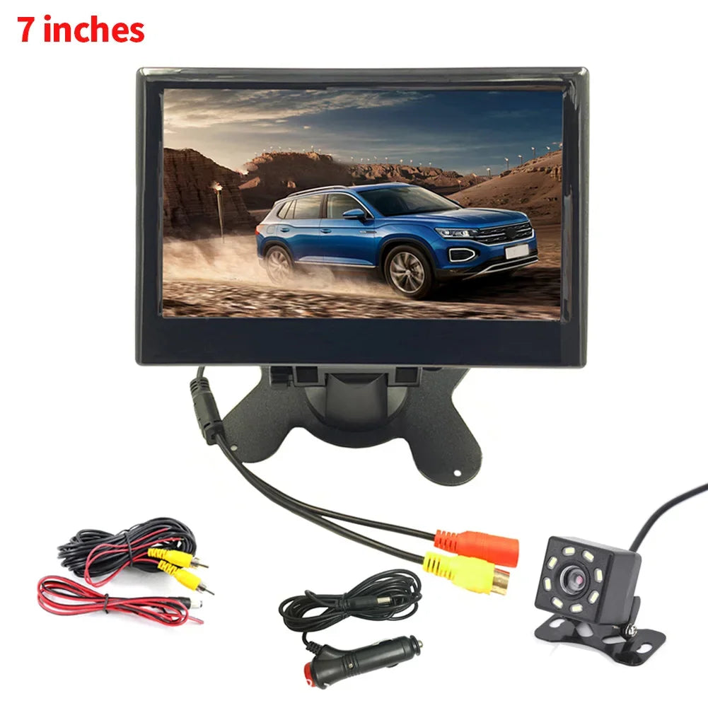 A 7-inch car monitor display showing a blue SUV on a dirt road. Includes a backup camera, power cables, and connectors against a white background.