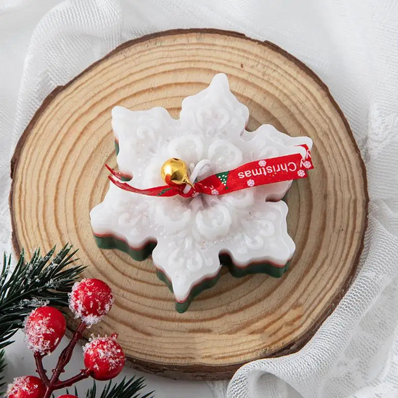 Snowflake-shaped soap on a wooden slice, adorned with a red "Christmas" ribbon and gold bell, next to snowy red berries and green leaves on a white fabric background.