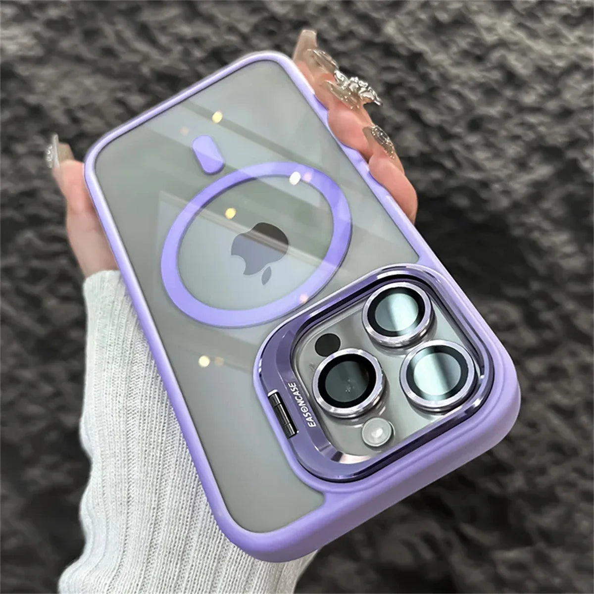 A person holding a smartphone with a lavender case featuring prominent camera lenses and a circular design on the back. The phone rests on a hand with long, decorated nails.