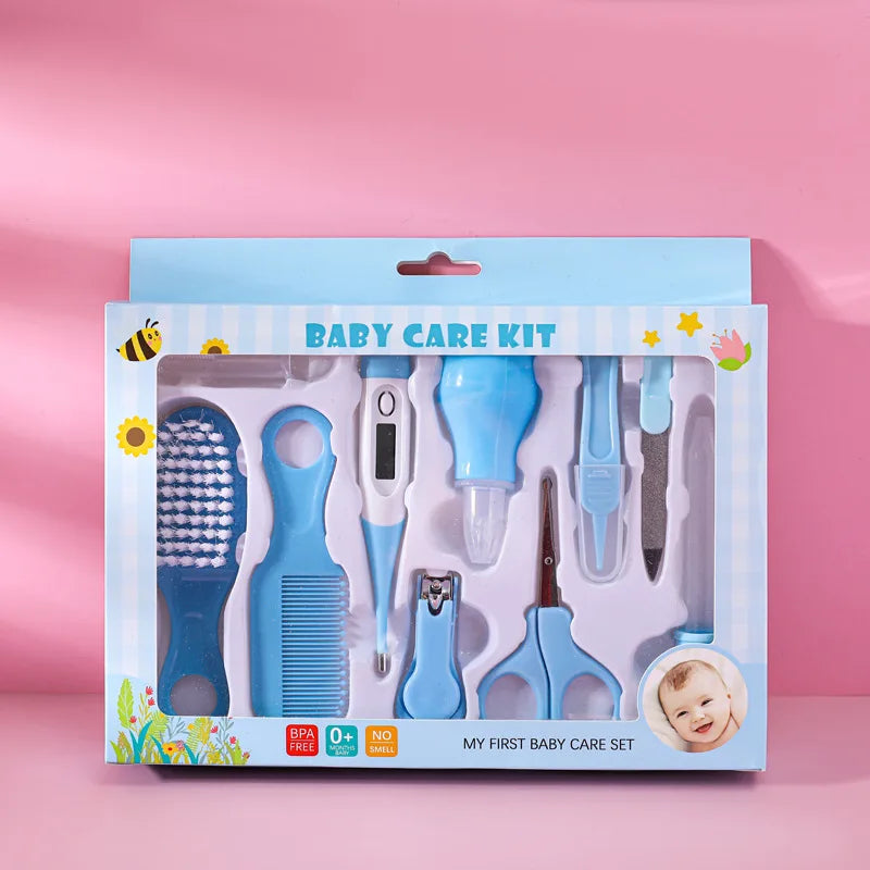 Blue and white baby care kit on a pink background. Includes a brush, comb, thermometer, nasal aspirator, nail clipper, scissors, and file. Packaging features "My First Baby Care Set."