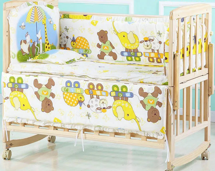 Wooden baby crib with wheels featuring colorful animal-themed bedding. Designs include bears, elephants, and letters. The crib is positioned against a pastel wall.