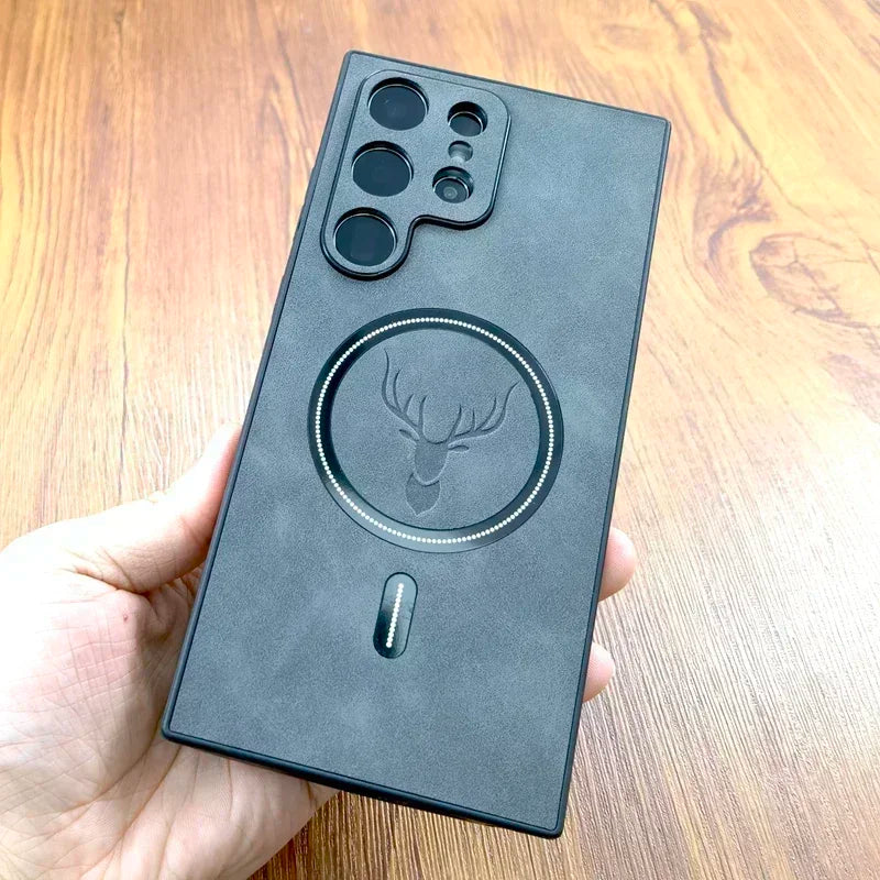 A person holds a black phone case with a deer emblem and large circular design on the back, featuring multiple camera cutouts. The case rests on a wooden surface.