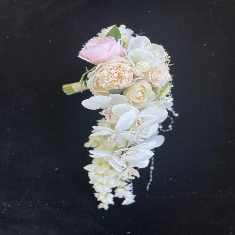 Cascading bouquet with pastel pink and peach roses, white orchids, and delicate greenery against a black background, creating a romantic and elegant arrangement.
