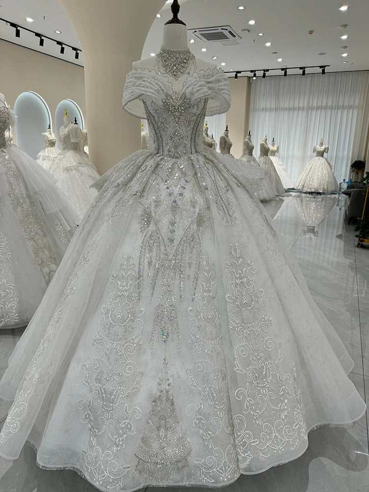 Ornate white wedding dress on a mannequin in a bridal boutique, featuring intricate beading and embroidery, with off-the-shoulder sleeves and a voluminous skirt.