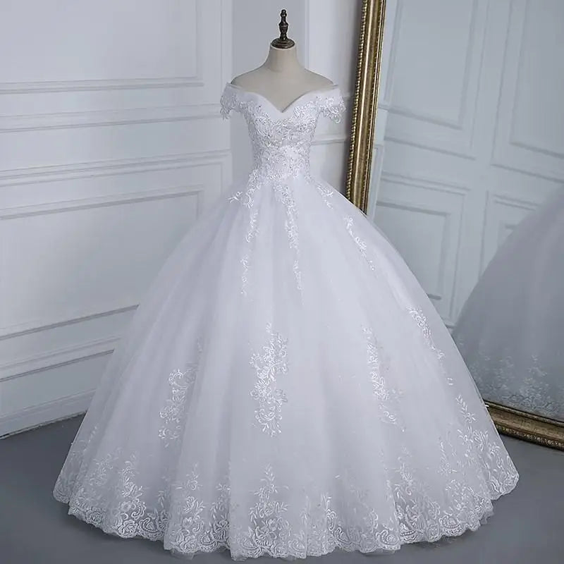 Elegant white off-shoulder wedding gown on a mannequin, featuring intricate lace details and a voluminous tulle skirt, placed beside a large ornate mirror.