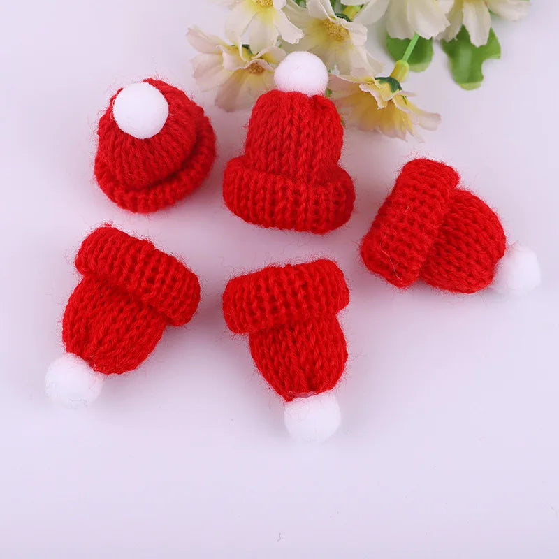 Five miniature red knit hats with white pom-poms are arranged in a circle on a light surface, with delicate white flowers partially visible in the background.