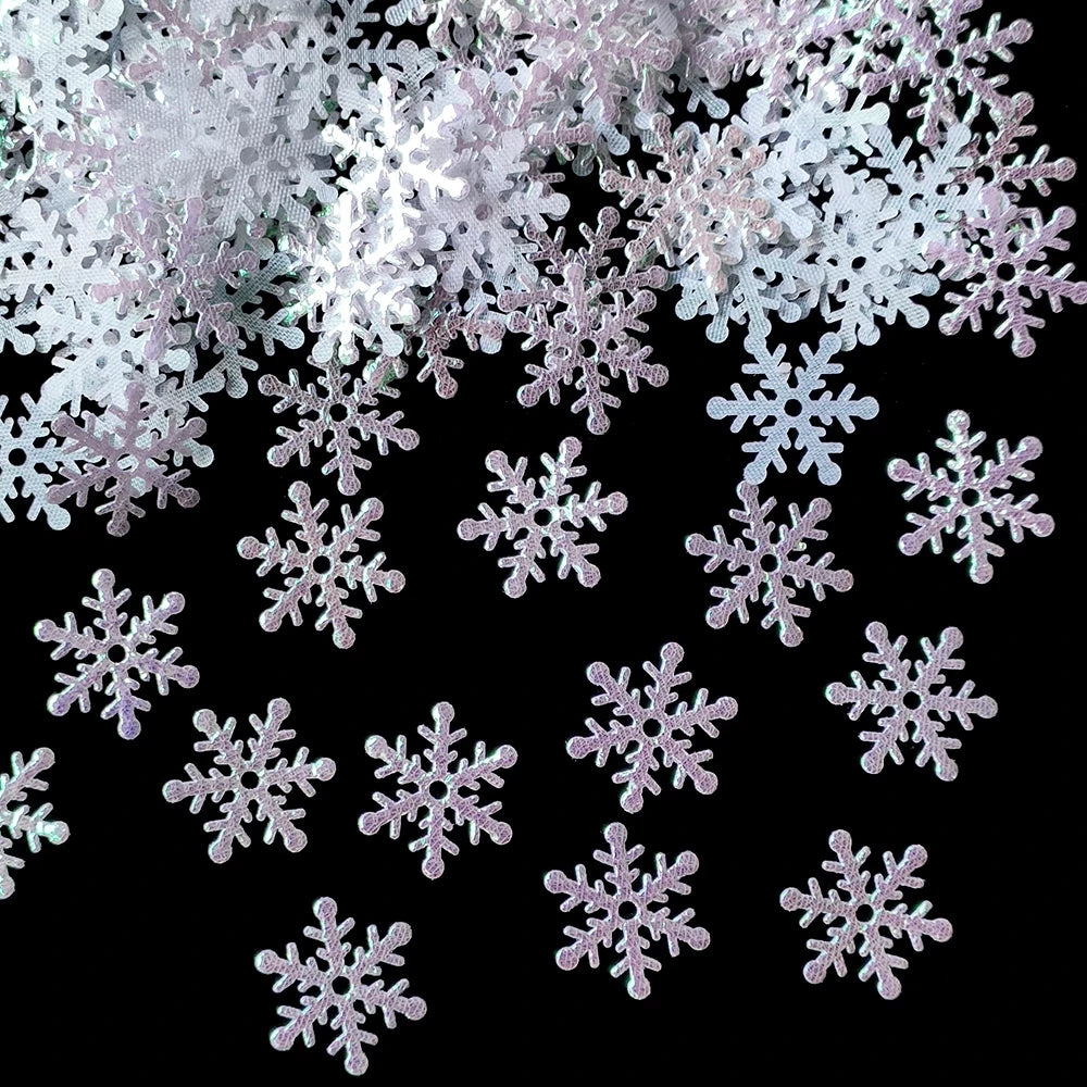 Glittery white and silver snowflake confetti scattered on a black background, creating a festive and wintry scene.