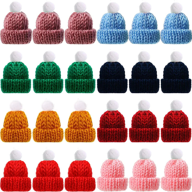 A collection of small knitted hats in various colors including pink, blue, green, navy, yellow, red, and rose. Each hat features a fluffy white pompom on top.