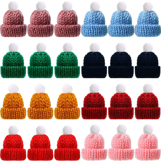 A collection of small knitted hats in various colors including pink, blue, green, navy, yellow, red, and rose. Each hat features a fluffy white pompom on top.