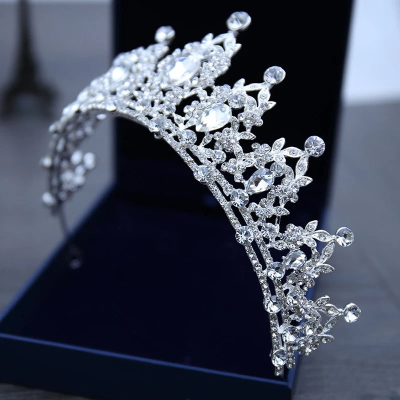 Silver tiara adorned with large teardrop and round crystals, displayed in an open blue velvet box, set against a blurred background.