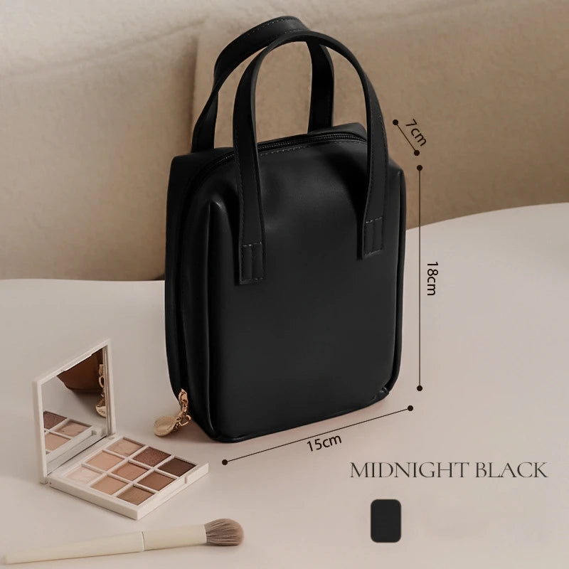 A black makeup bag with two handles is displayed on a table, measuring 18cm by 15cm by 7cm. Nearby are a compact mirror, eyeshadow palette, and makeup brush.