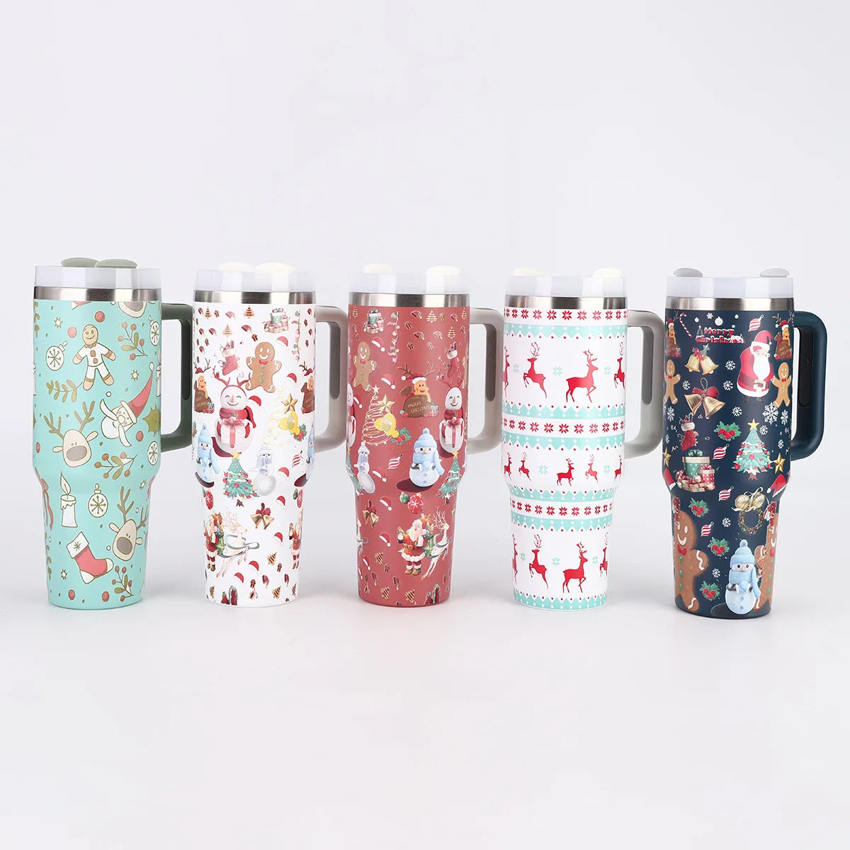 Five travel mugs with festive holiday designs, featuring gingerbread men, snowmen, reindeer, and Christmas trees, stand side by side against a plain white background.