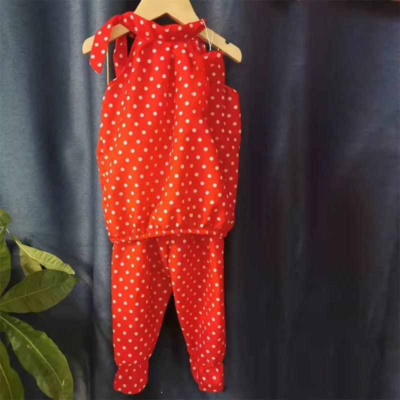 Red children's outfit with white polka dots, featuring a halter top and matching pants hanging on a wooden hanger, set against a dark background.