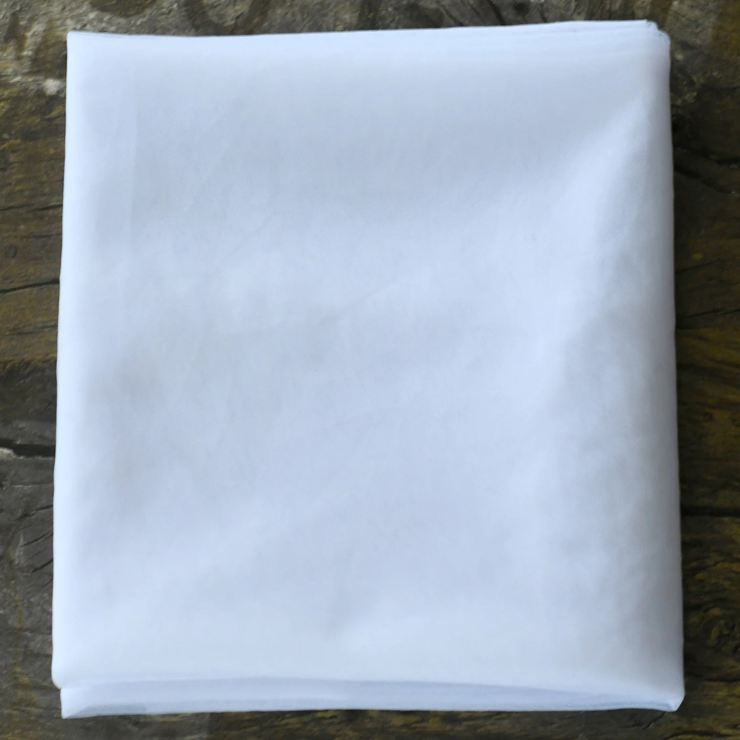 A neatly folded white fabric square lies on a textured wooden surface, showcasing its crisp and clean appearance.
