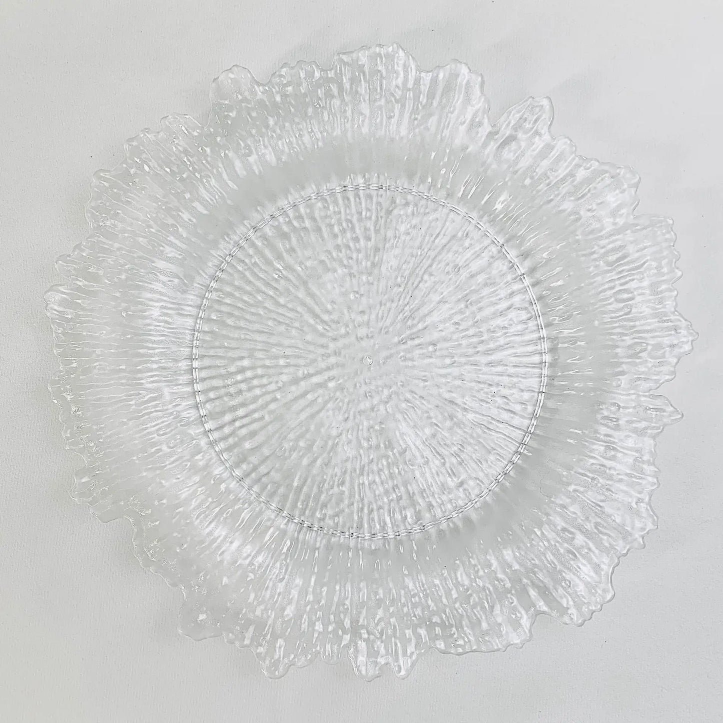 A textured, clear glass plate with a jagged, decorative edge resembling a sunburst pattern, viewed from above against a plain white background.