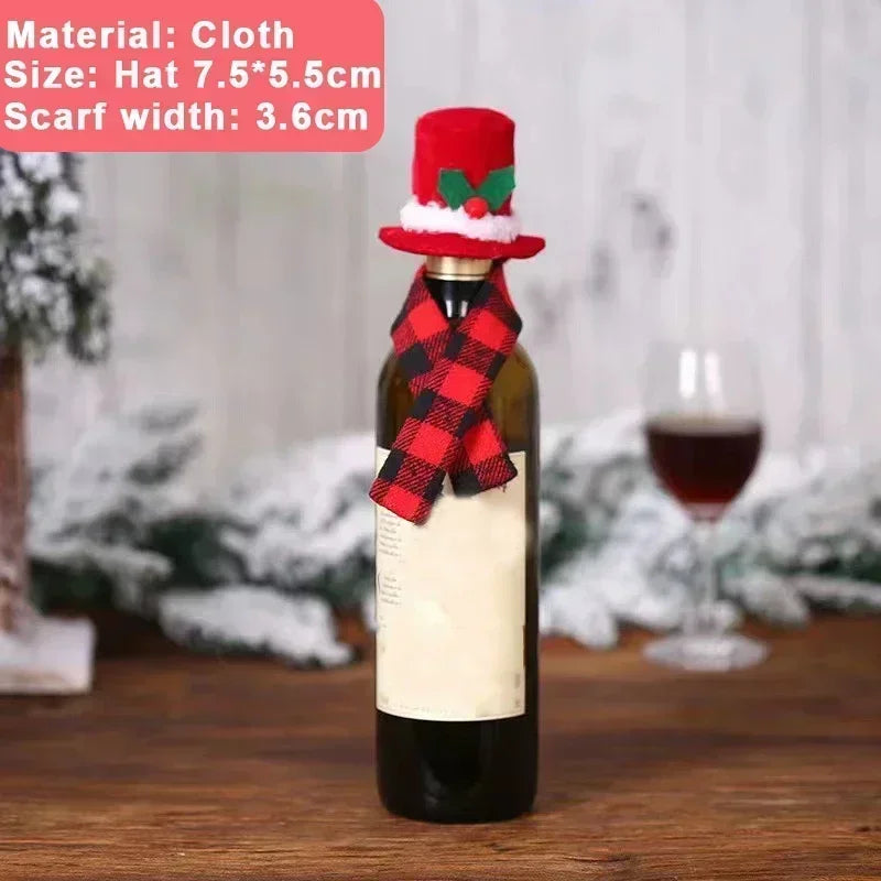 A wine bottle dressed with a red and green holiday hat and a red plaid scarf. Background features a wooden table, snowy branches, and a blurred wine glass.