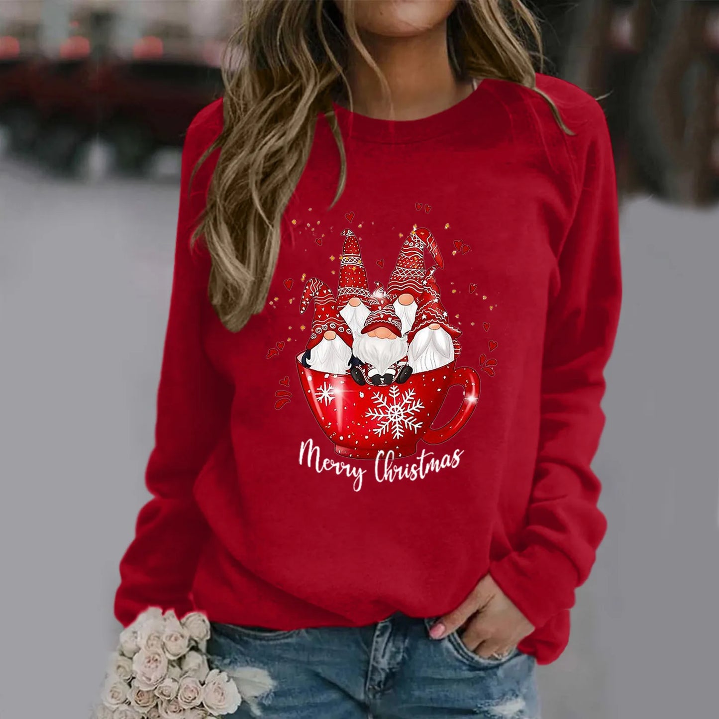 Woman in red Christmas sweatshirt with gnome design and "Merry Christmas" text, holding white roses. The sweater features gnomes in a festive red mug with snowflakes.