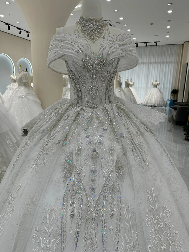 A luxurious white wedding gown adorned with intricate silver embellishments and sparkling crystals, displayed on a mannequin in an elegant bridal showroom.