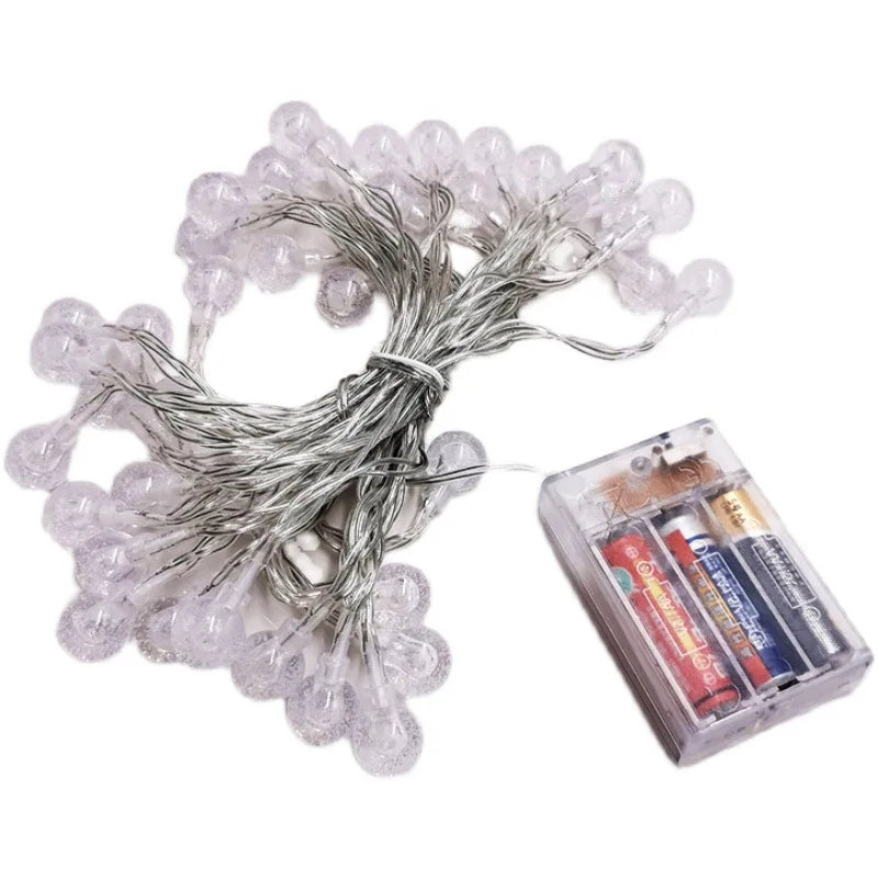 String of clear, round fairy lights with textured bulbs, coiled next to a transparent battery pack containing three AA batteries.