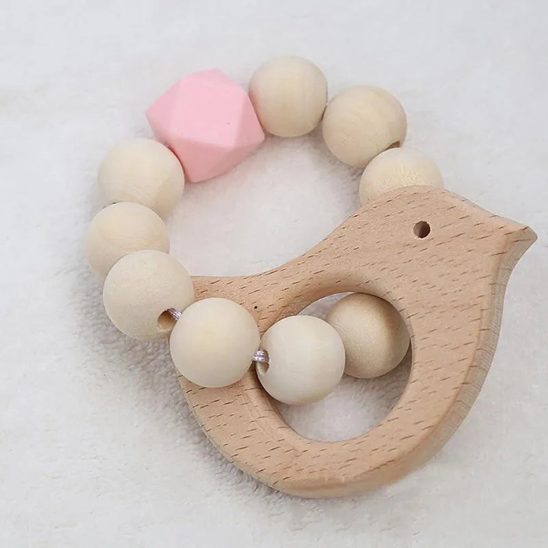 Wooden bird-shaped teether with round beads, one pink geometric bead, on a soft white surface. Natural and baby-friendly design suitable for infants.