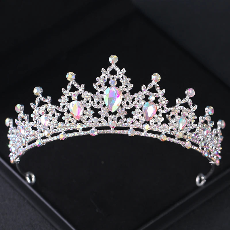 A sparkling silver tiara adorned with clear and iridescent gemstones in intricate patterns, set against a black background.