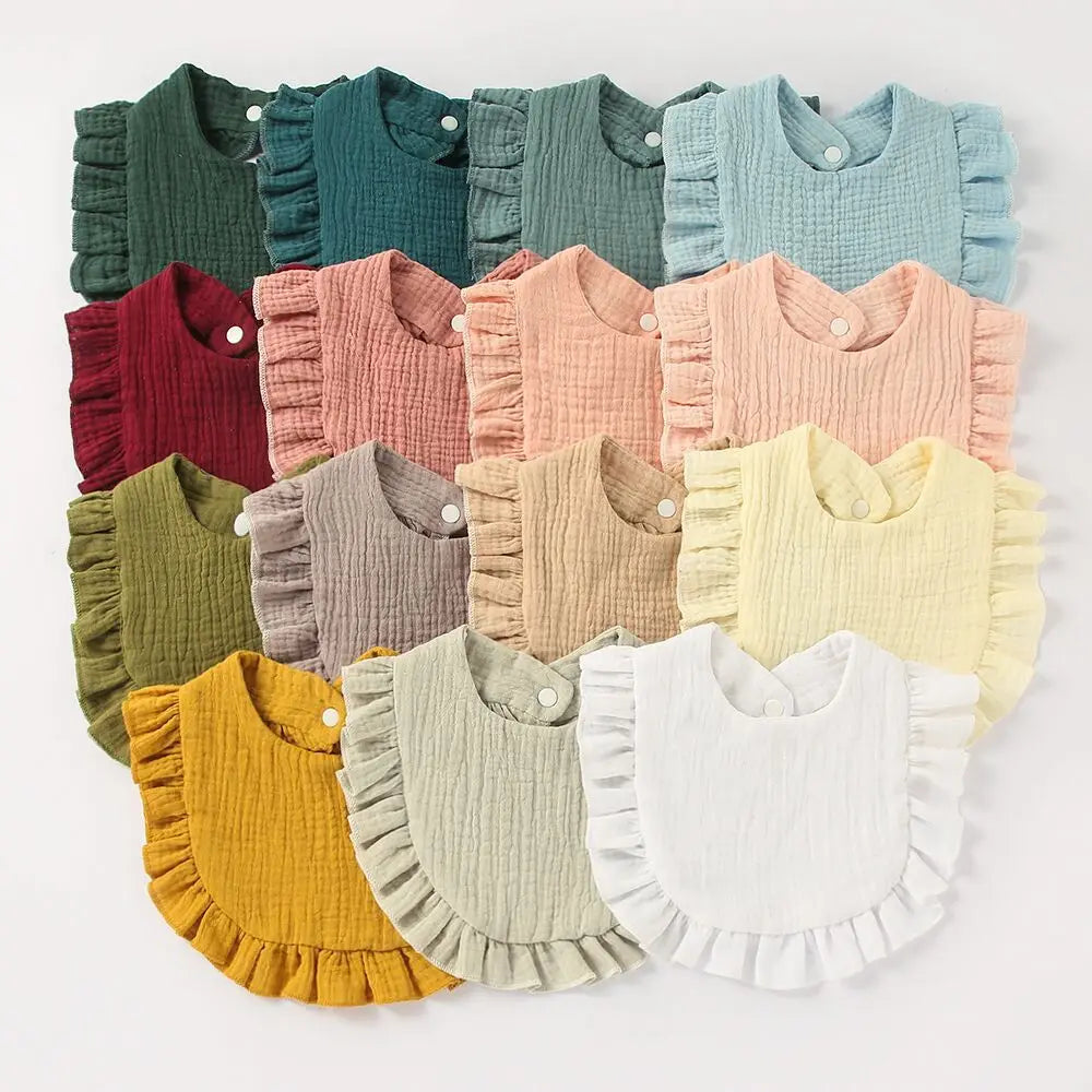 A collection of 15 ruffled baby bibs in various colors, including shades of green, blue, red, pink, mustard yellow, and white, neatly arranged on a flat surface.