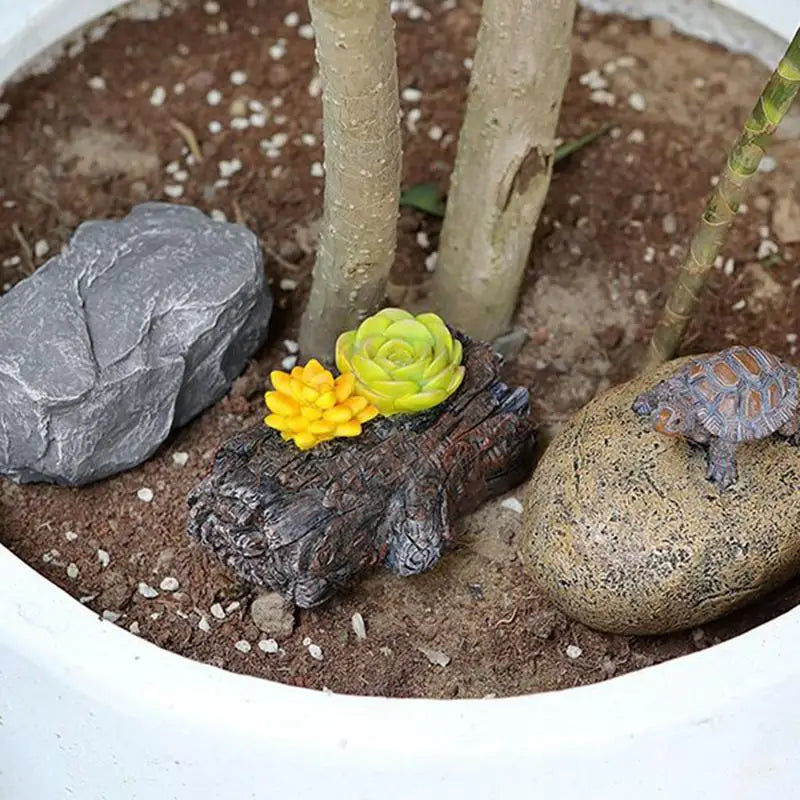 Miniature garden with a decorative rock, a log with yellow and green succulents, and a stone with a small turtle figurine, placed in a white pot with soil.