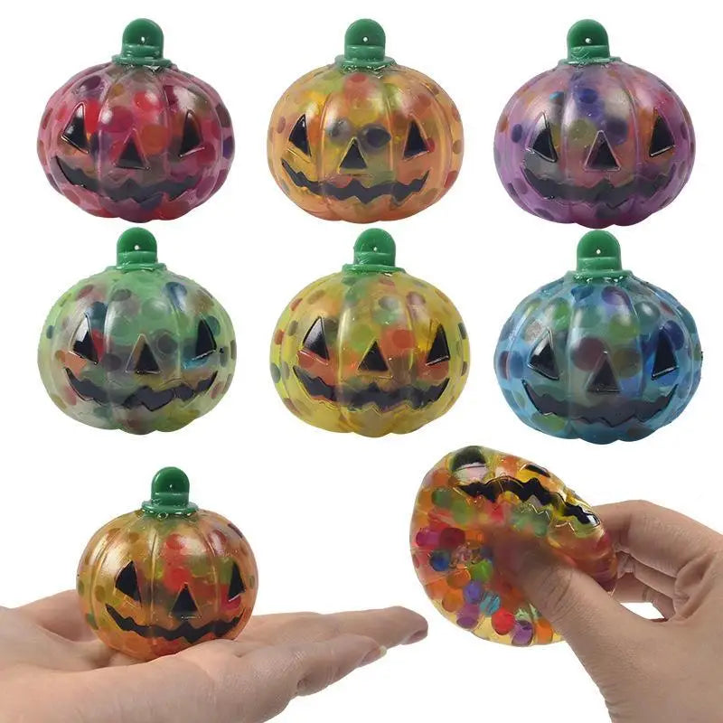 Colorful pumpkin-shaped stress balls with jack-o'-lantern faces, filled with multicolored orbs. One is being squeezed in a hand, showing the soft texture.