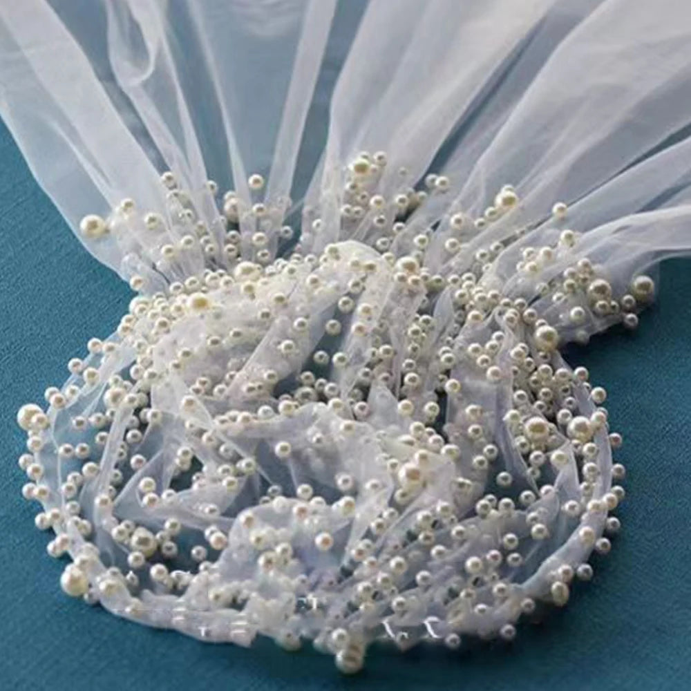 Sheer white fabric adorned with numerous small pearls, elegantly gathered on a blue surface, creating a delicate and luxurious texture.