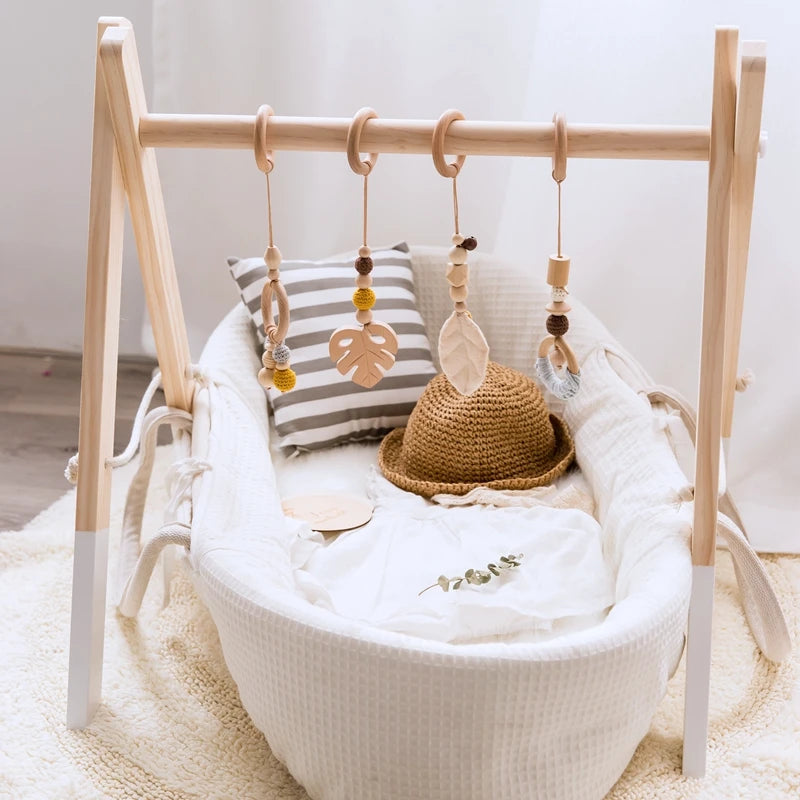 Wooden baby bassinet with a natural-colored crochet hat, striped cushion, and a hanging mobile above with leaf-shaped and bead ornaments on a white and cozy blanket.